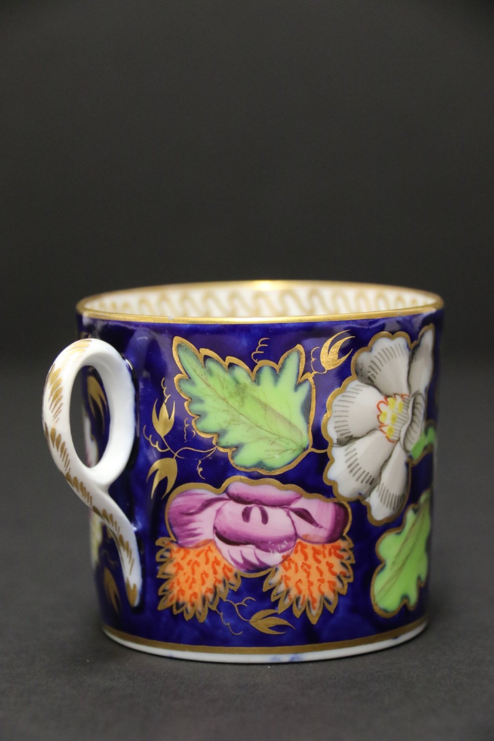 An early 19th-century English Newhall porcelain cabinet trio with a cobalt blue ground, hand-painted botanical flowers, and gilded borders. View XIV