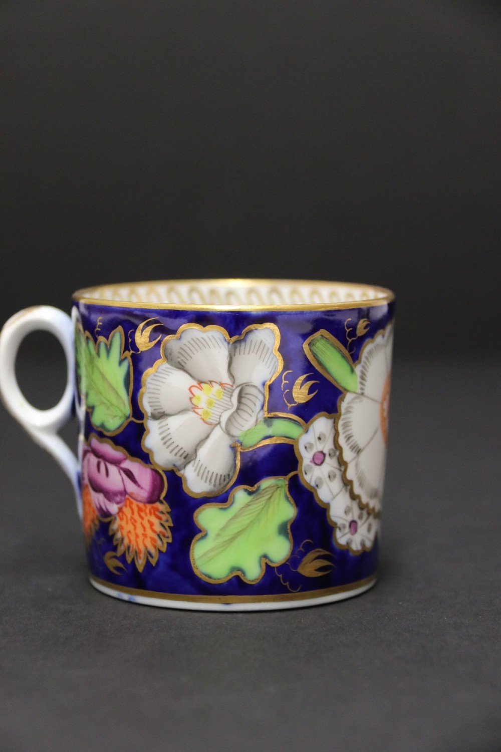 An early 19th-century English Newhall porcelain cabinet trio with a cobalt blue ground, hand-painted botanical flowers, and gilded borders. View XV