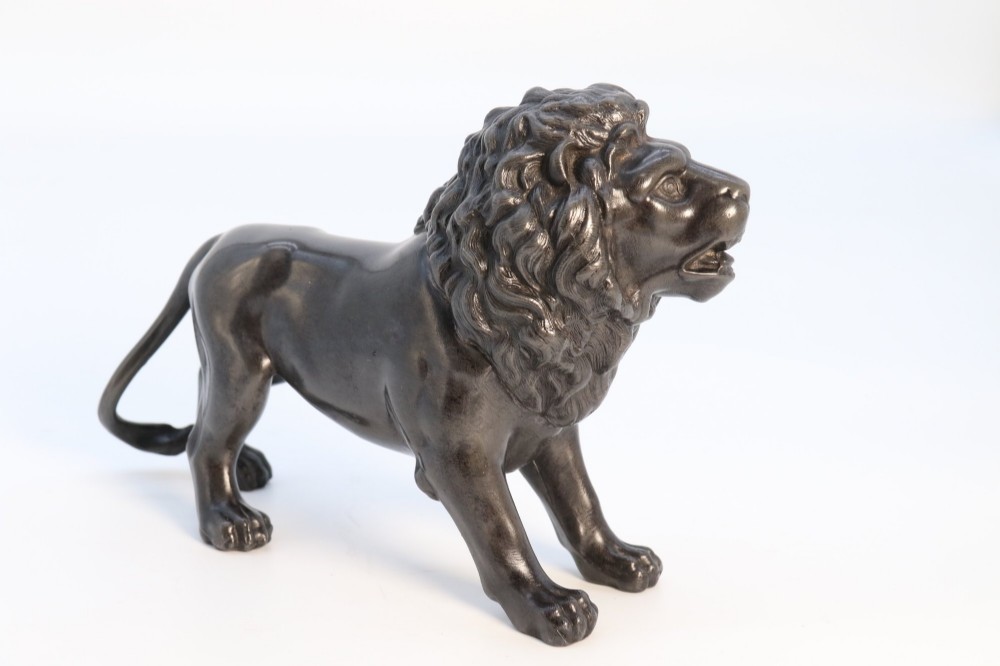 A dark patinated pewter sculpture depicting a standing male lion with a flowing mane and open mouth.
