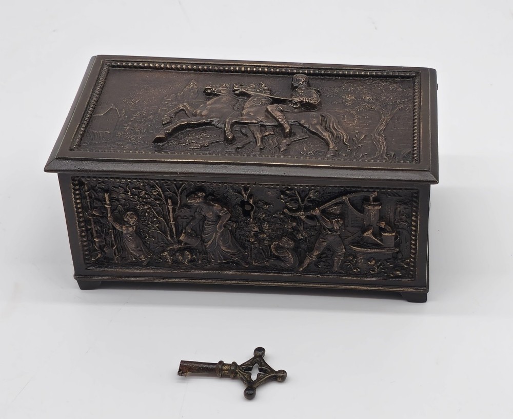 A dark patinated bronze rectangular jewellery casket featuring raised relief scenes of horses on the lid and rural figures on the side, displayed with its key.