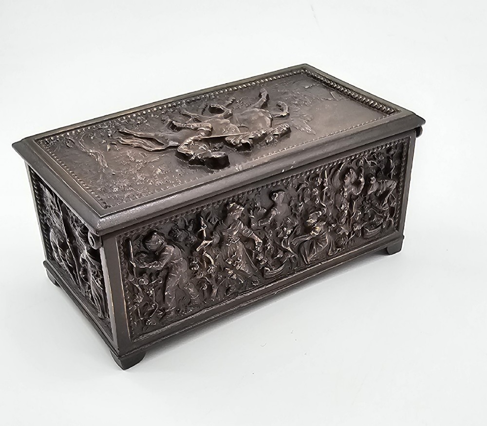 A dark patinated bronze rectangular jewellery casket featuring raised relief scenes of horses on the lid and rural figures on the side, displayed with its key. View II