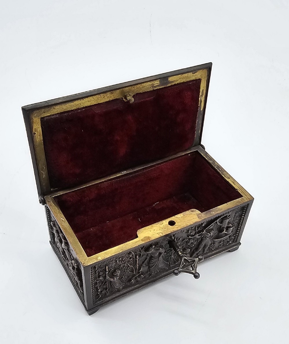 A dark patinated bronze rectangular jewellery casket featuring raised relief scenes of horses on the lid and rural figures on the side, displayed with its key. View III