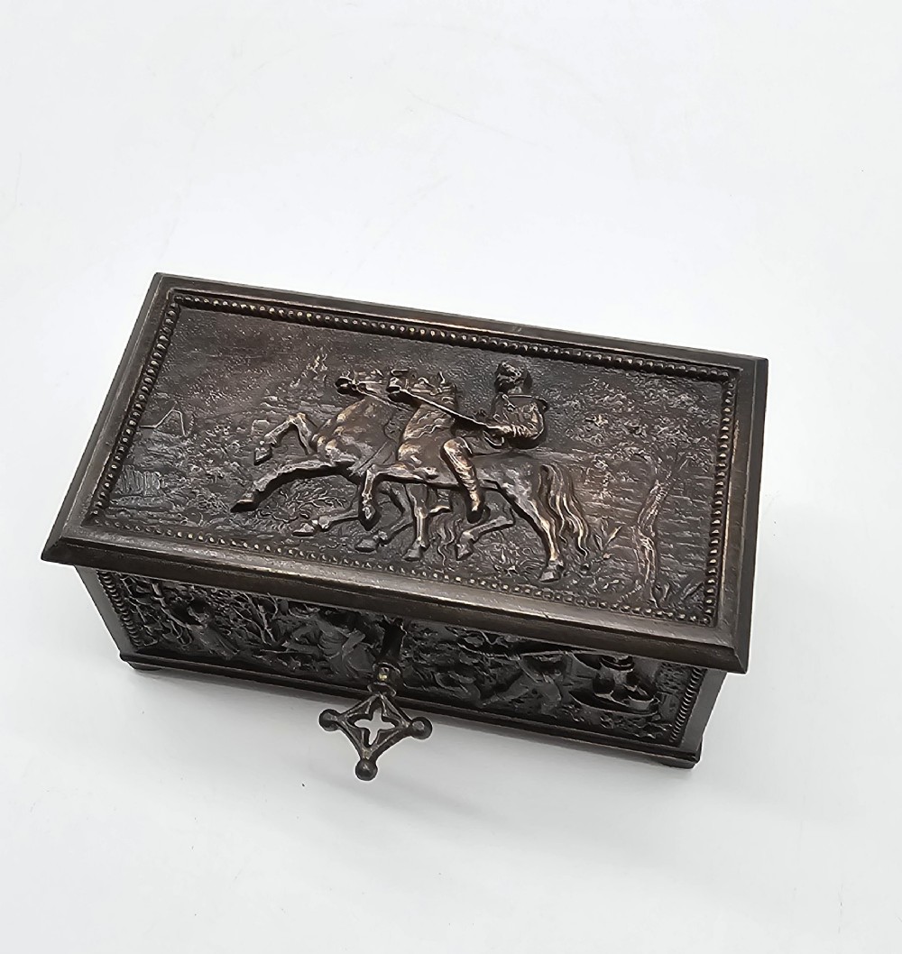 A dark patinated bronze rectangular jewellery casket featuring raised relief scenes of horses on the lid and rural figures on the side, displayed with its key. View V