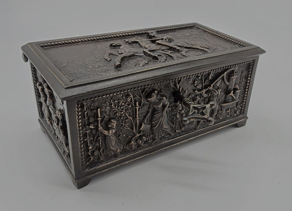 A dark patinated bronze rectangular jewellery casket featuring raised relief scenes of horses on the lid and rural figures on the side, displayed with its key. View VI