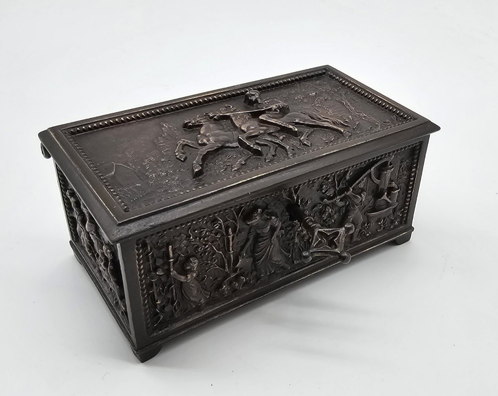 A dark patinated bronze rectangular jewellery casket featuring raised relief scenes of horses on the lid and rural figures on the side, displayed with its key. View VII