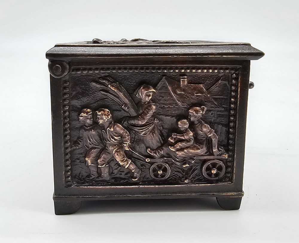 A dark patinated bronze rectangular jewellery casket featuring raised relief scenes of horses on the lid and rural figures on the side, displayed with its key. View VIII