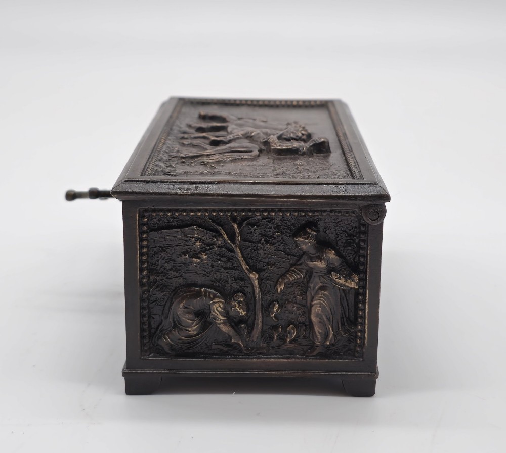 A dark patinated bronze rectangular jewellery casket featuring raised relief scenes of horses on the lid and rural figures on the side, displayed with its key. View X