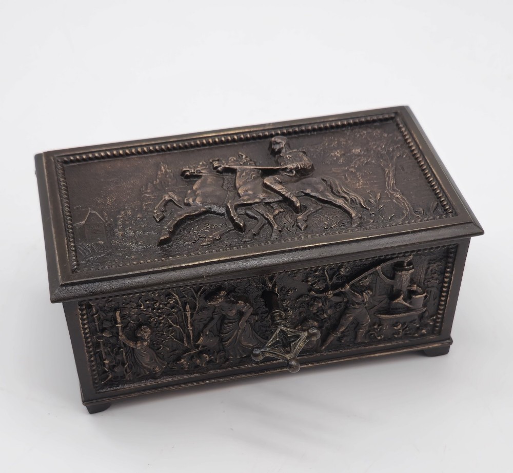 A dark patinated bronze rectangular jewellery casket featuring raised relief scenes of horses on the lid and rural figures on the side, displayed with its key. View XI