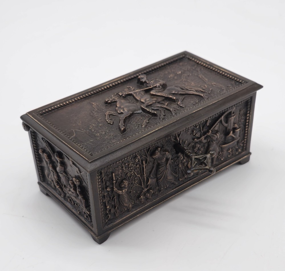 A dark patinated bronze rectangular jewellery casket featuring raised relief scenes of horses on the lid and rural figures on the side, displayed with its key. View XII