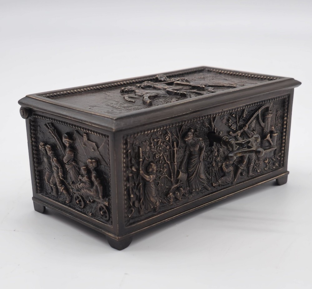 A dark patinated bronze rectangular jewellery casket featuring raised relief scenes of horses on the lid and rural figures on the side, displayed with its key. View XIII