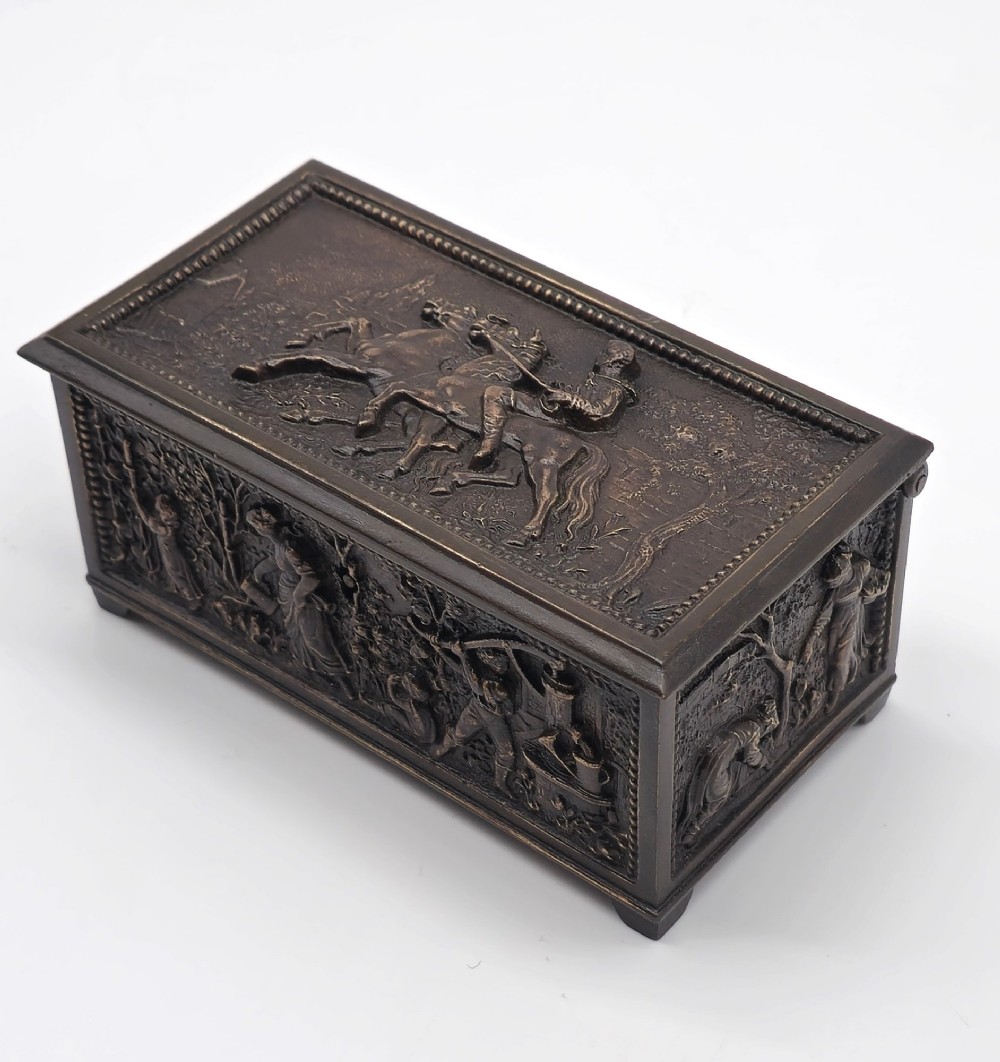 A dark patinated bronze rectangular jewellery casket featuring raised relief scenes of horses on the lid and rural figures on the side, displayed with its key. View XV