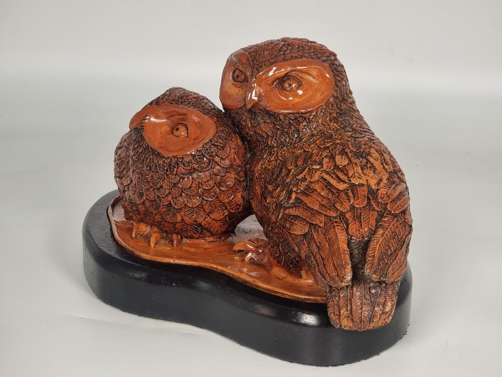 A hand-sculpted warm brown pottery pair of owls featuring textured feather detailing resting on an oval ebonised wooden base. View VII