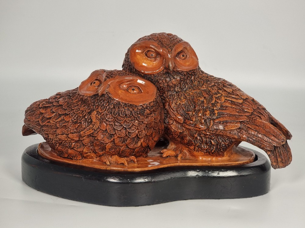 A hand-sculpted warm brown pottery pair of owls featuring textured feather detailing resting on an oval ebonised wooden base. View VIII