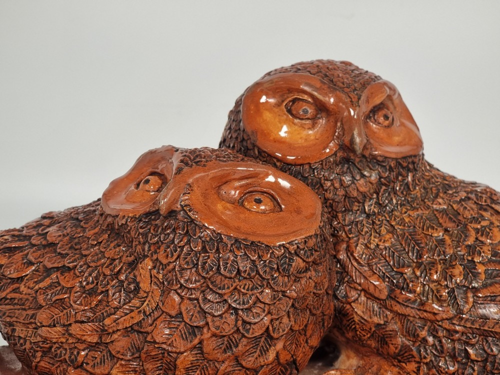 A hand-sculpted warm brown pottery pair of owls featuring textured feather detailing resting on an oval ebonised wooden base. View IX