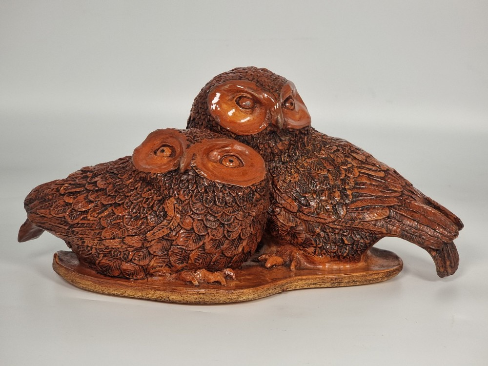 A hand-sculpted warm brown pottery pair of owls featuring textured feather detailing resting on an oval ebonised wooden base. View XI