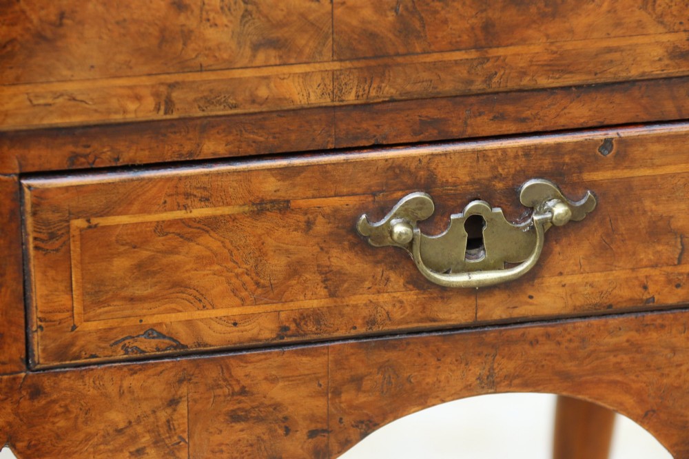 A George II burr elm lowboy table with three drawers, brass handles, a shaped apron, and cabriole legs. View V