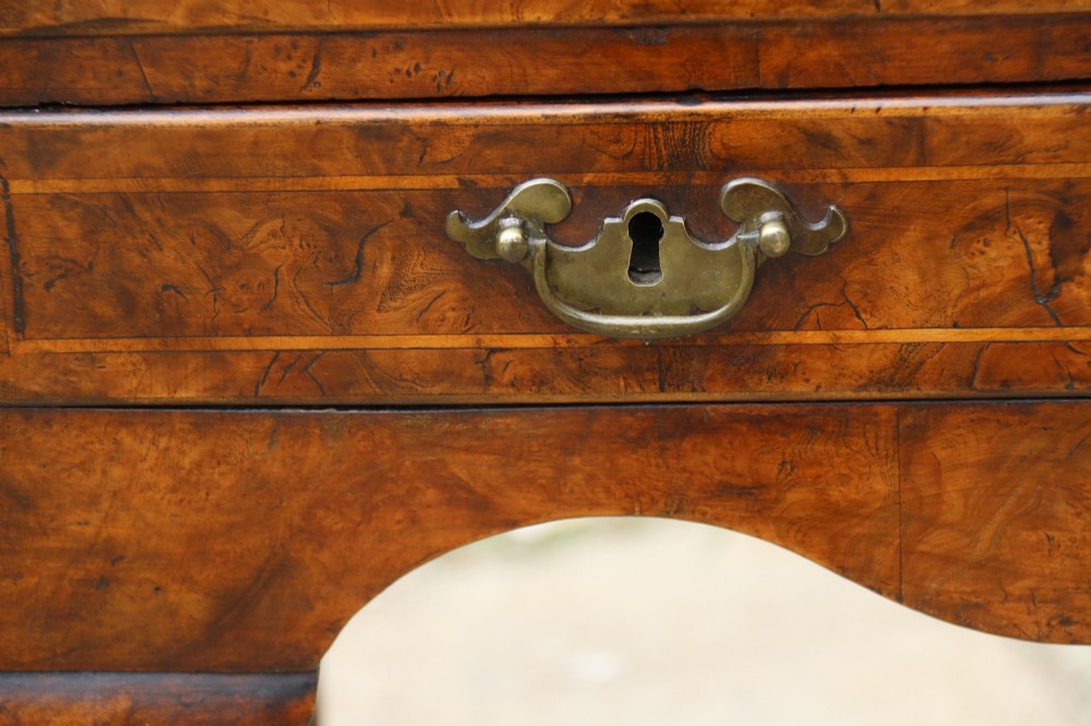 A George II burr elm lowboy table with three drawers, brass handles, a shaped apron, and cabriole legs. View VI