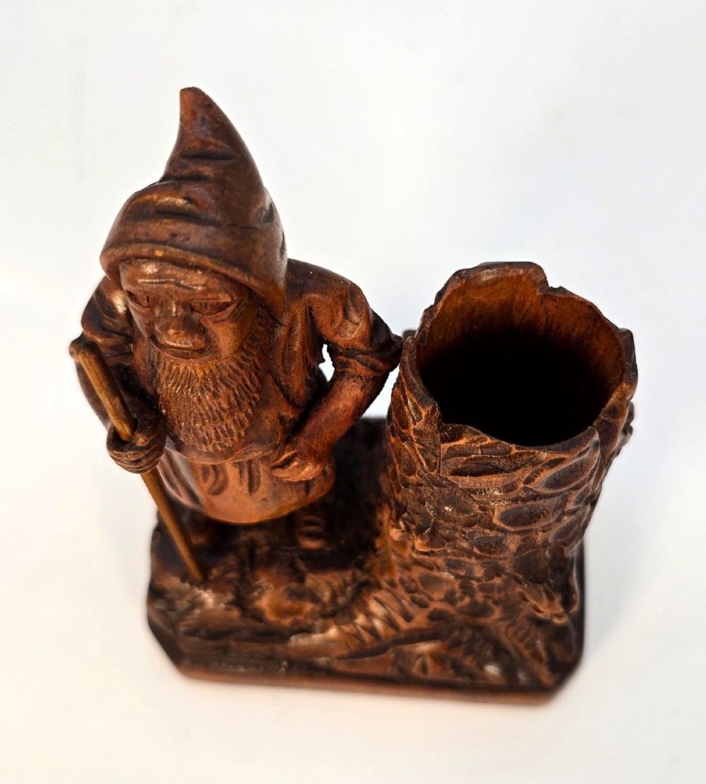 A carved brown limewood match holder depicting a hooded bearded gnome standing beside a textured tree stump container. View XIII