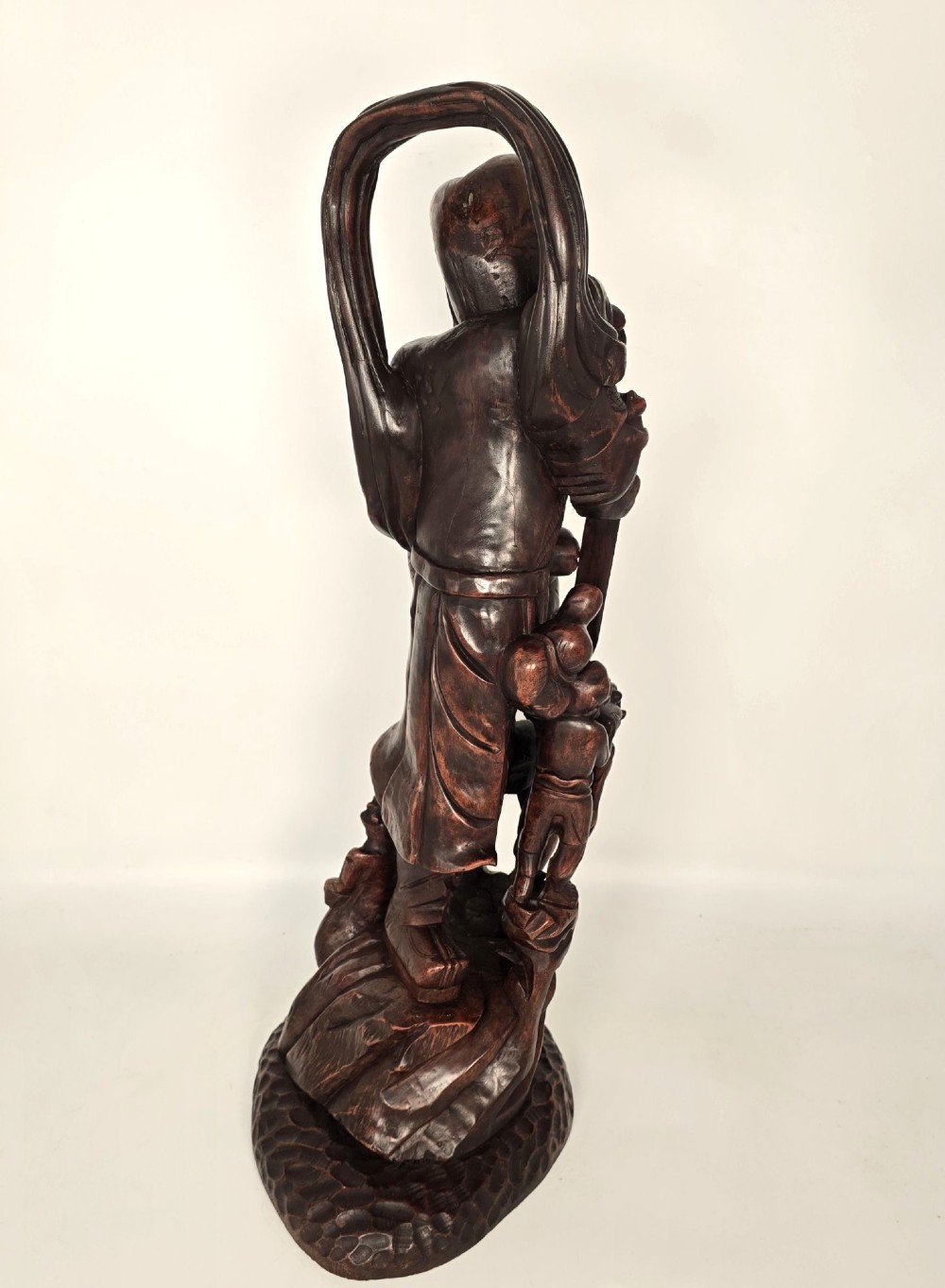 A tall carved dark hardwood Chinese sculpture depicting a Guardian King wearing detailed armour and holding a sword over attendant figures. View V