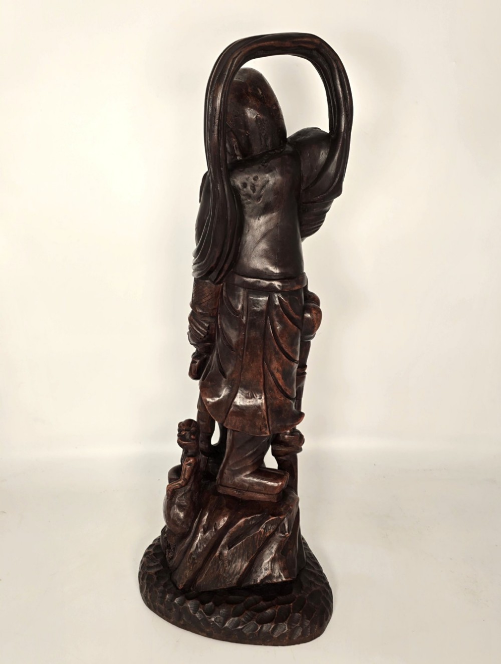 A tall carved dark hardwood Chinese sculpture depicting a Guardian King wearing detailed armour and holding a sword over attendant figures. View VI