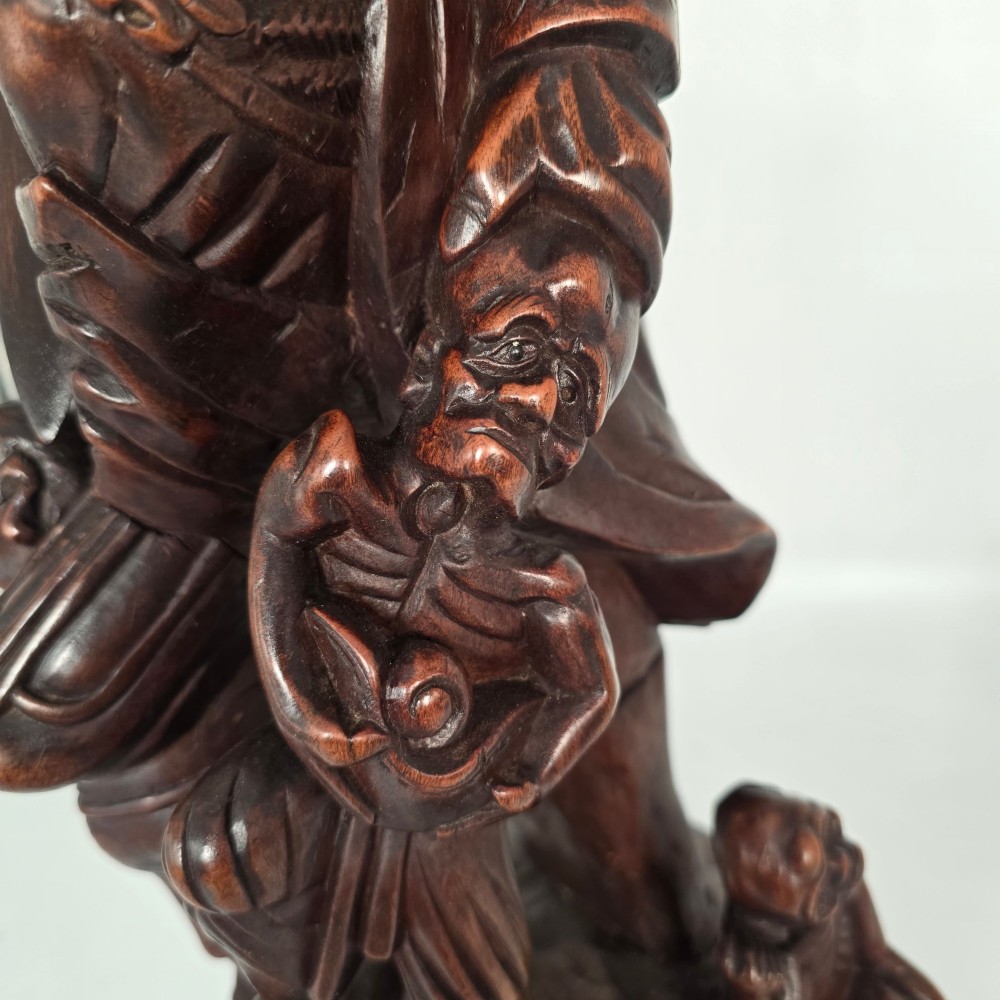 A tall carved dark hardwood Chinese sculpture depicting a Guardian King wearing detailed armour and holding a sword over attendant figures. View IX
