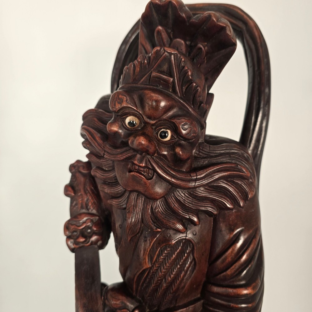 A tall carved dark hardwood Chinese sculpture depicting a Guardian King wearing detailed armour and holding a sword over attendant figures. View XI