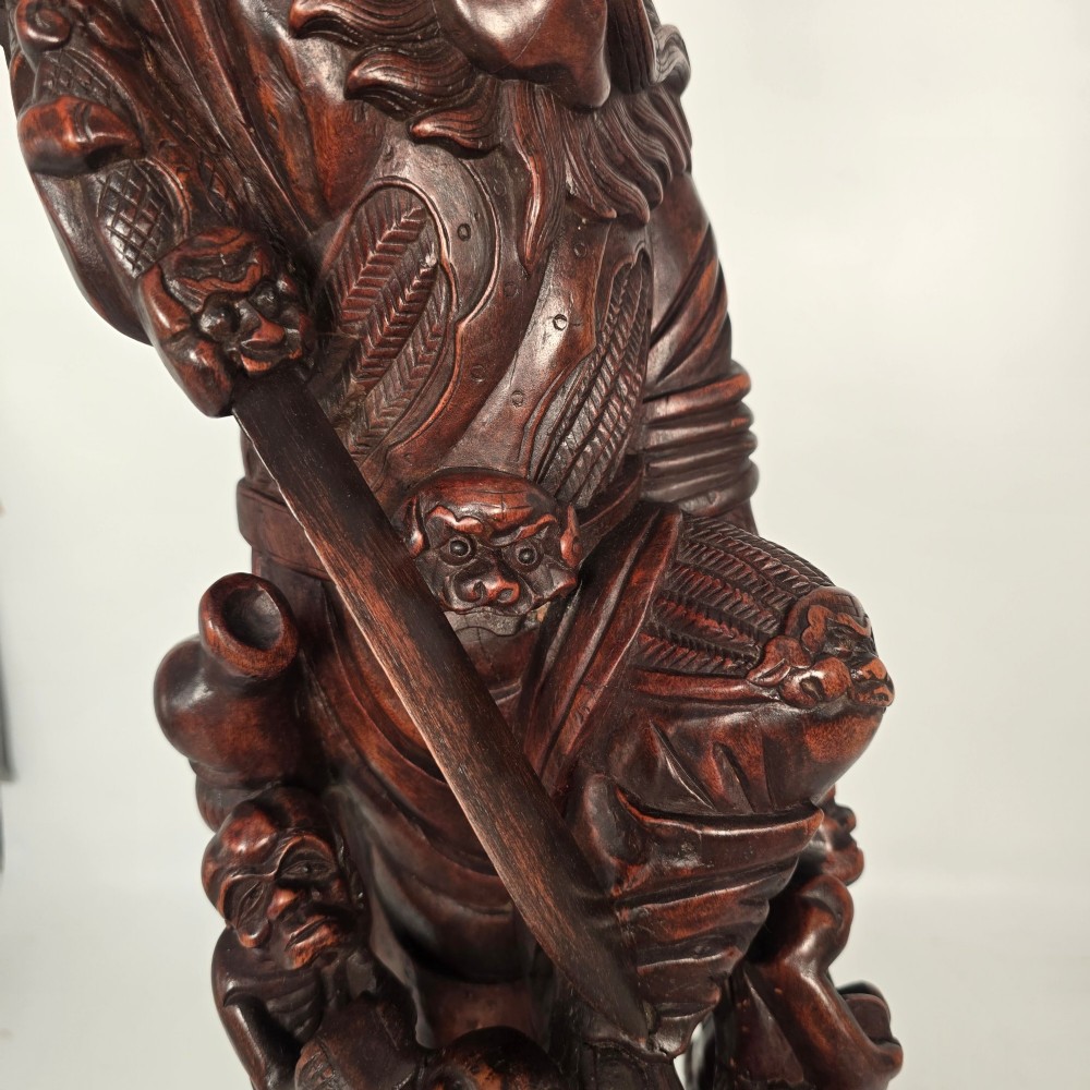 A tall carved dark hardwood Chinese sculpture depicting a Guardian King wearing detailed armour and holding a sword over attendant figures. View XIII