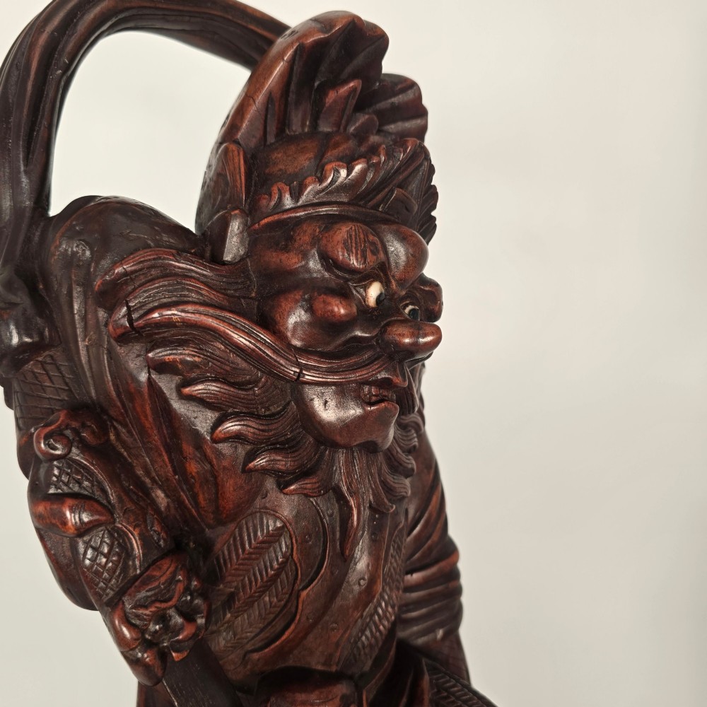 A tall carved dark hardwood Chinese sculpture depicting a Guardian King wearing detailed armour and holding a sword over attendant figures. View XIV
