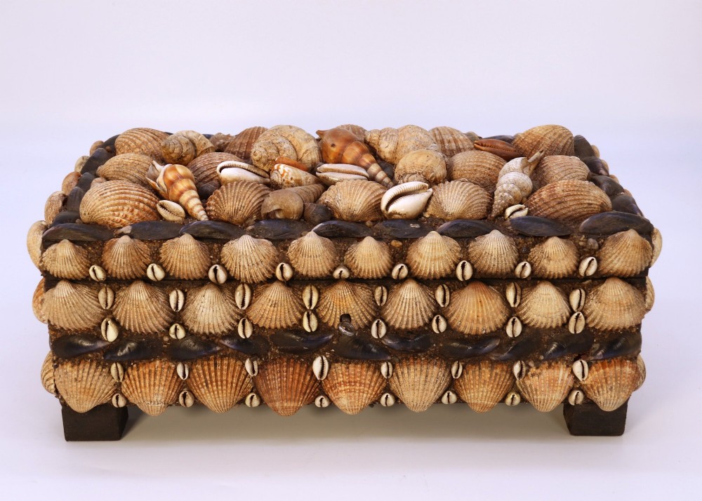 A rectangular wooden box encrusted entirely with an assortment of natural seashells, supported by four short block feet. View II
