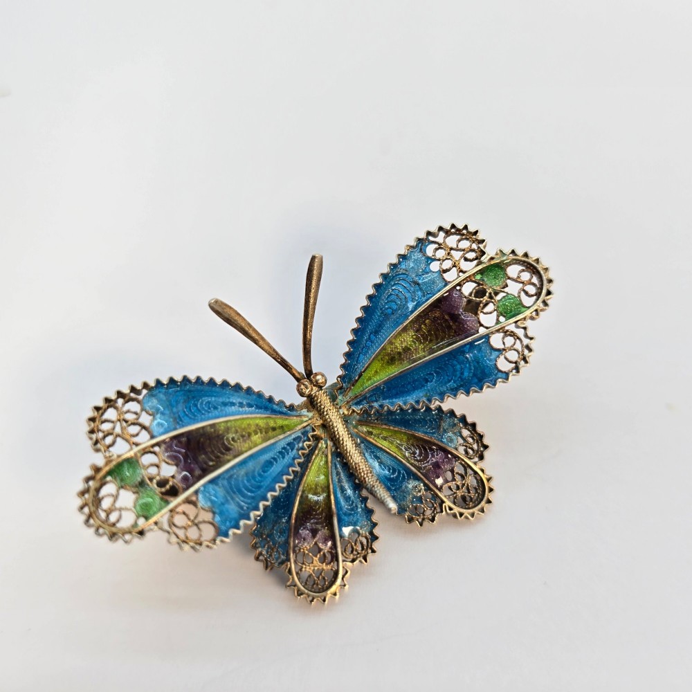 An Art Deco silver gilt butterfly brooch featuring blue, green, and purple enamel panels edged with wire filigree. View II