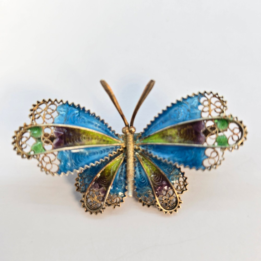 An Art Deco silver gilt butterfly brooch featuring blue, green, and purple enamel panels edged with wire filigree. View V
