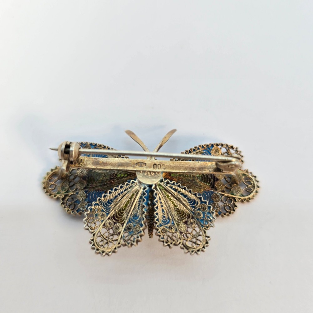 An Art Deco silver gilt butterfly brooch featuring blue, green, and purple enamel panels edged with wire filigree. View VI