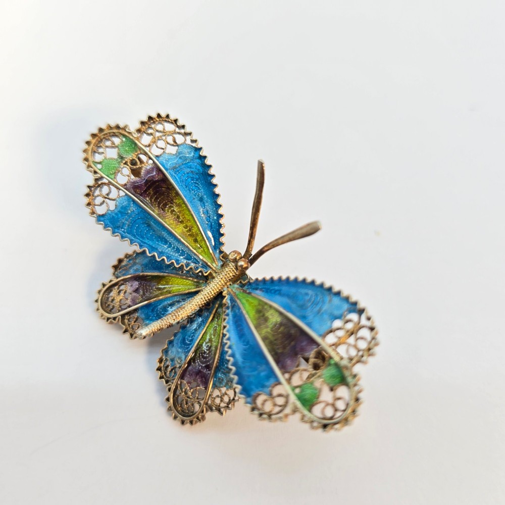 An Art Deco silver gilt butterfly brooch featuring blue, green, and purple enamel panels edged with wire filigree. View VIII