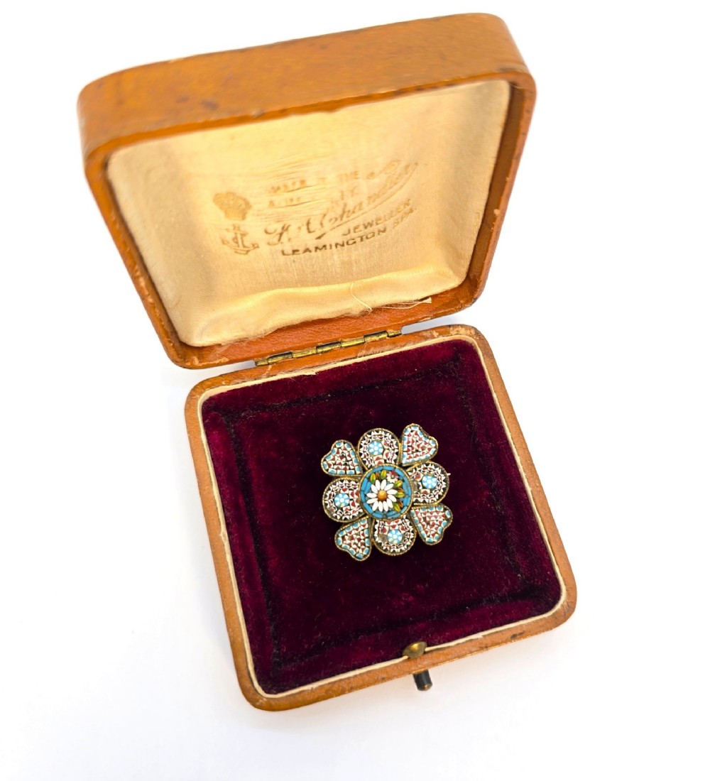 A floral-shaped 19th-century Italian micro mosaic brooch featuring colourful glass tesserae set inside an open velvet-lined tan leather box.