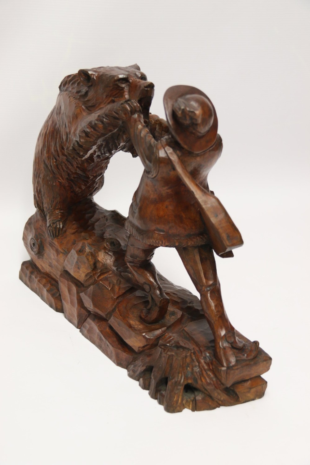 A detailed 19th-century carved walnut sculpture depicting a man in traditional attire struggling with a standing bear upon a carved log base. View II