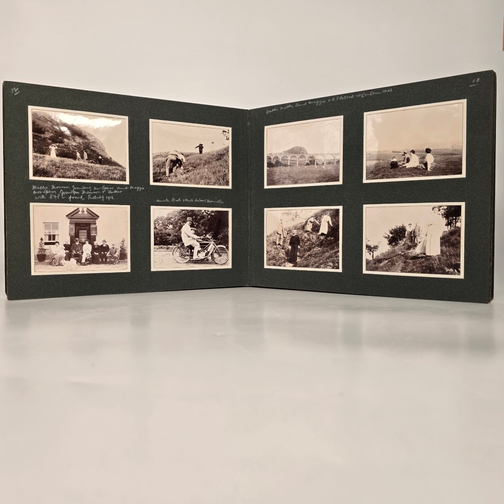 A set of three dark green cloth-bound Edwardian photograph albums stacked diagonally, featuring gold-embossed lettering and a geometric motif. View V