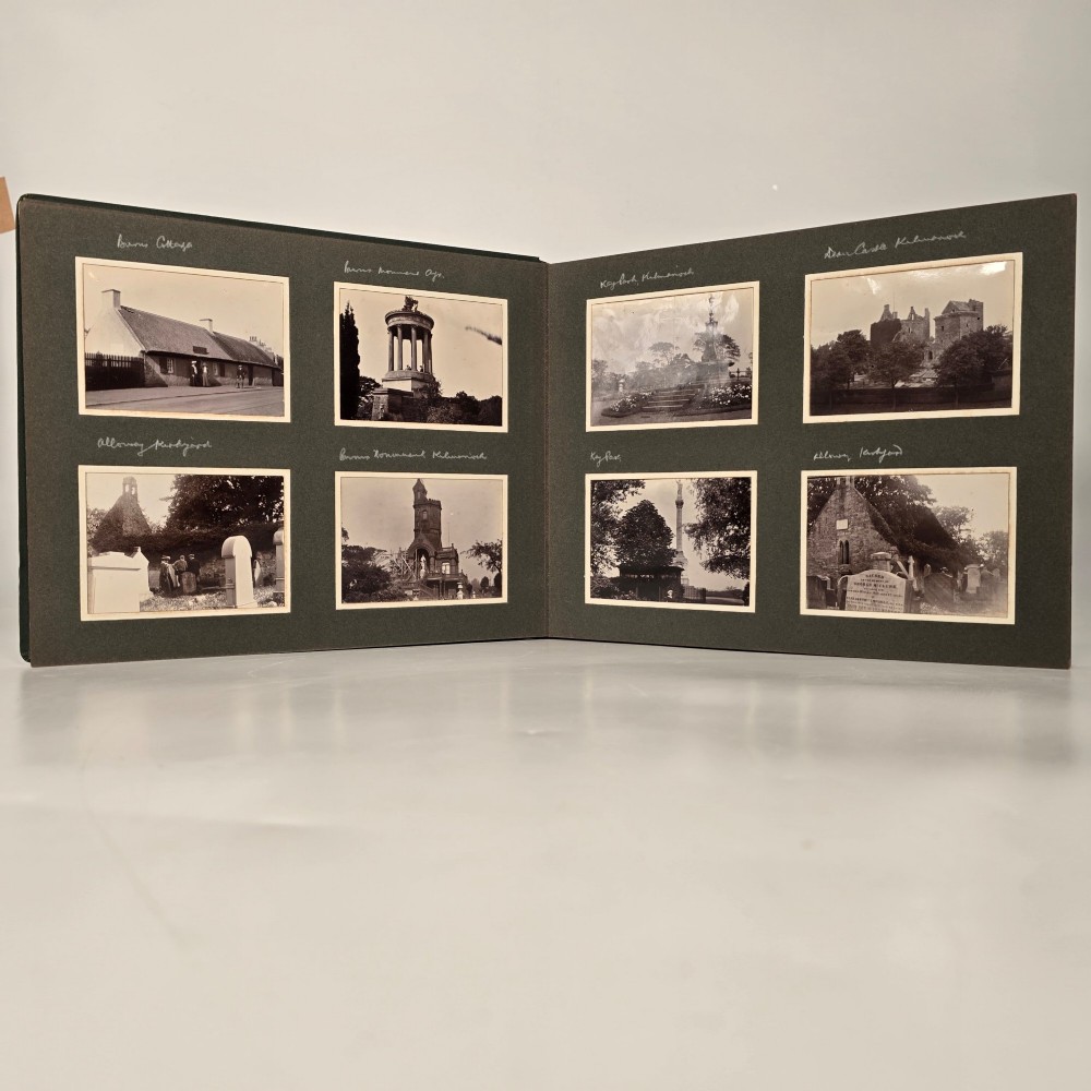 A set of three dark green cloth-bound Edwardian photograph albums stacked diagonally, featuring gold-embossed lettering and a geometric motif. View VII