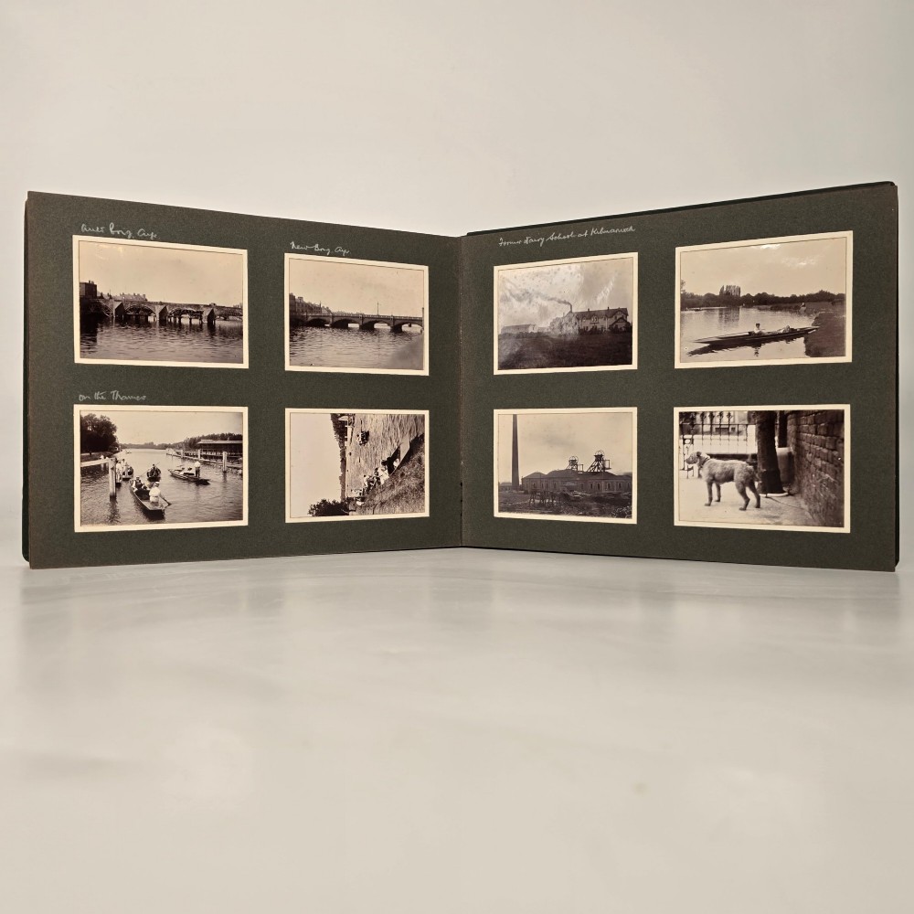 A set of three dark green cloth-bound Edwardian photograph albums stacked diagonally, featuring gold-embossed lettering and a geometric motif. View X