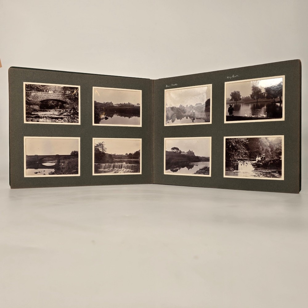 A set of three dark green cloth-bound Edwardian photograph albums stacked diagonally, featuring gold-embossed lettering and a geometric motif. View XII