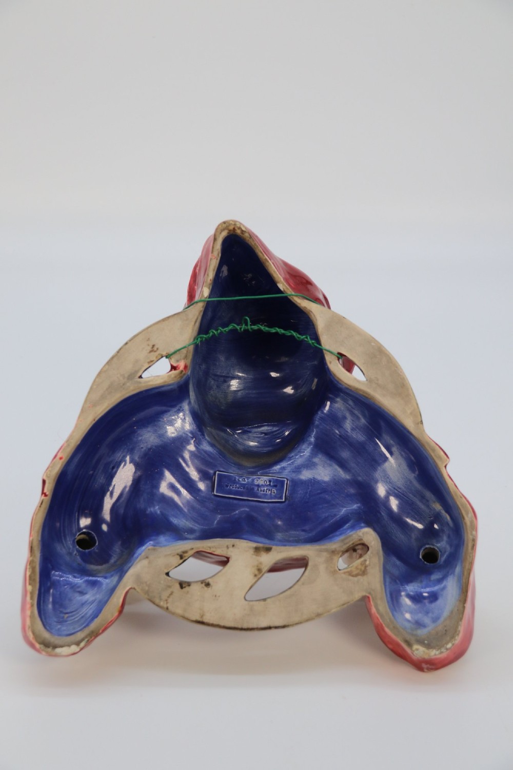 A glazed ceramic wall-mounted candelabra depicting a hooded monk in a red cowl holding two candle sockets. View X