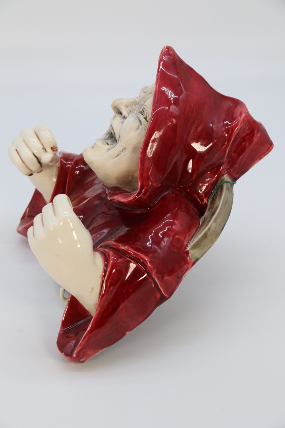 A glazed ceramic wall-mounted candelabra depicting a hooded monk in a red cowl holding two candle sockets. View XI
