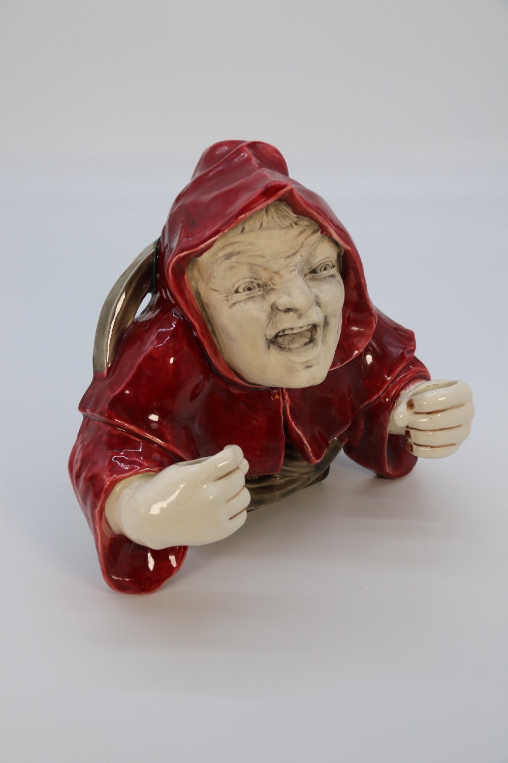 A glazed ceramic wall-mounted candelabra depicting a hooded monk in a red cowl holding two candle sockets. View XII