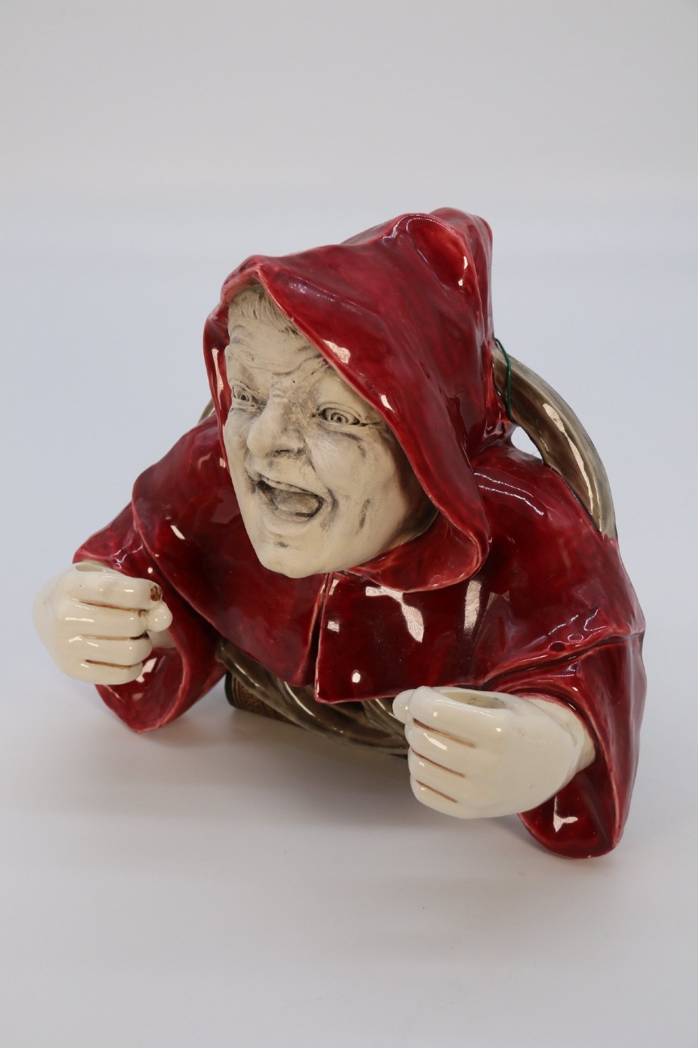 A glazed ceramic wall-mounted candelabra depicting a hooded monk in a red cowl holding two candle sockets. View XIII