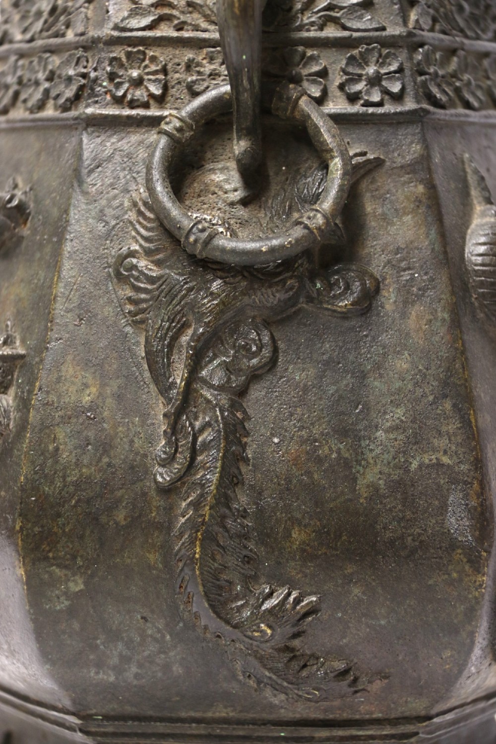 An antique hexagonal solid bronze vessel featuring relief carvings of fish, architectural structures, floral bands, and twin animal-head ring handles. View V