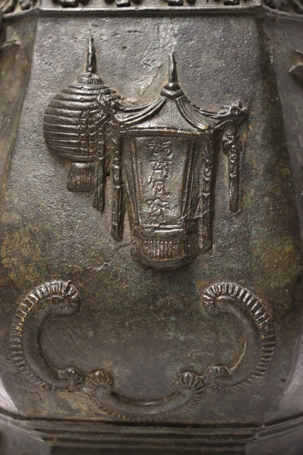 An antique hexagonal solid bronze vessel featuring relief carvings of fish, architectural structures, floral bands, and twin animal-head ring handles. View VII