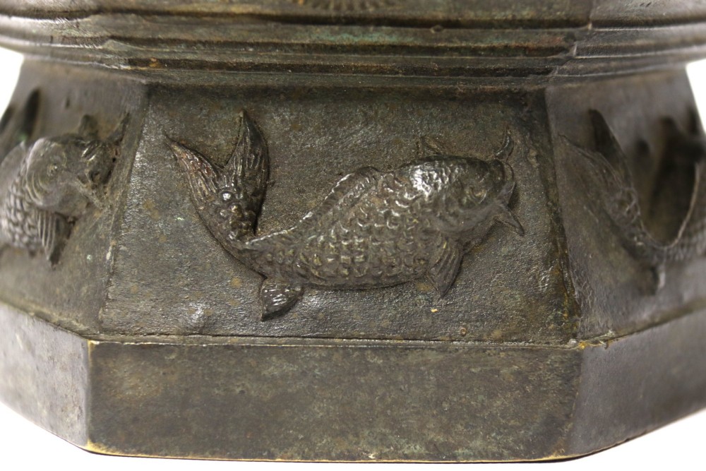 An antique hexagonal solid bronze vessel featuring relief carvings of fish, architectural structures, floral bands, and twin animal-head ring handles. View VIII