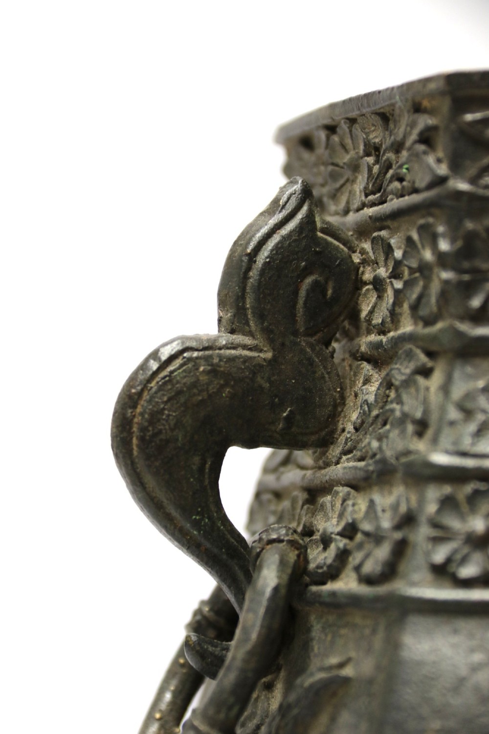 An antique hexagonal solid bronze vessel featuring relief carvings of fish, architectural structures, floral bands, and twin animal-head ring handles. View X