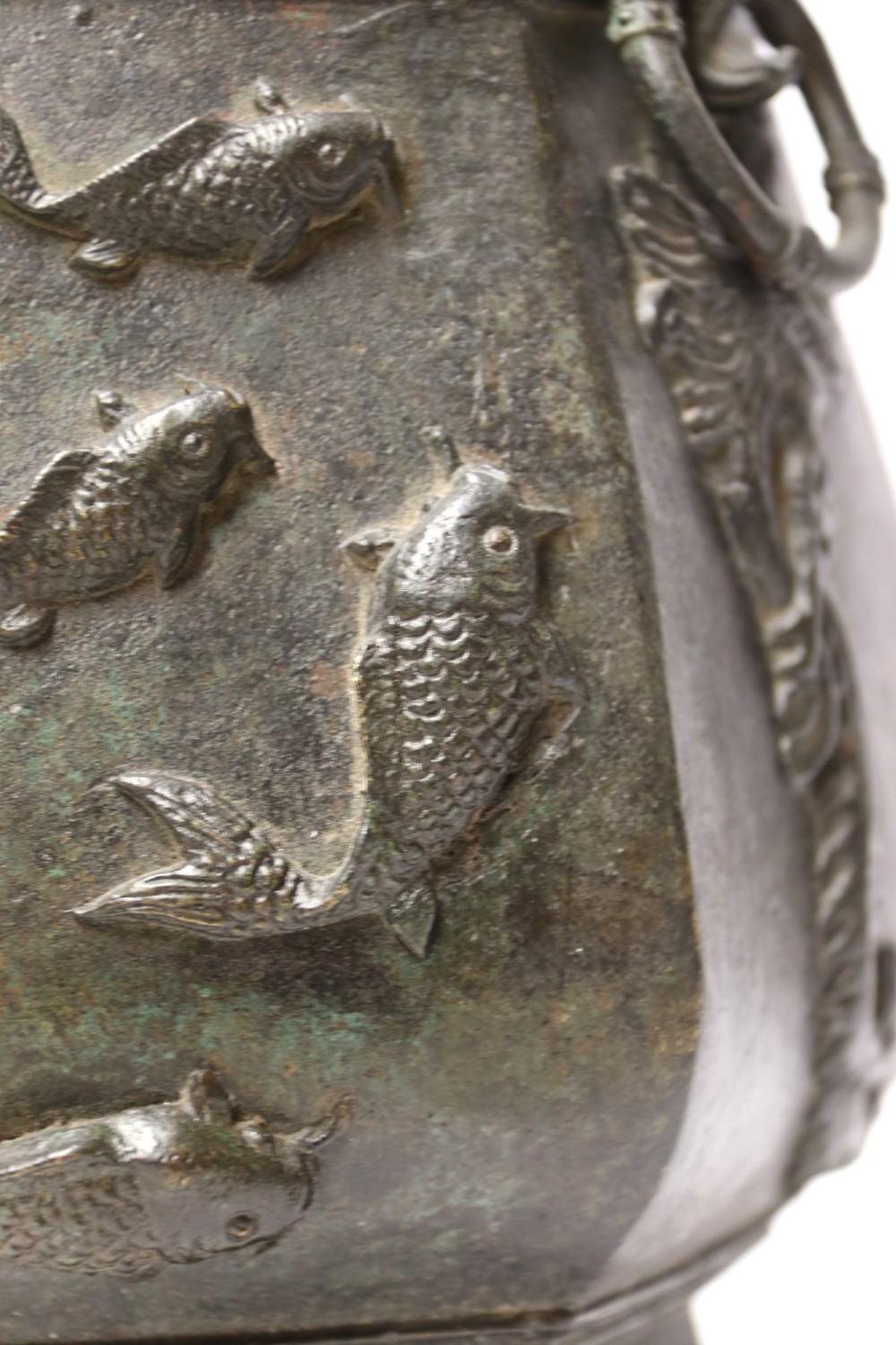 An antique hexagonal solid bronze vessel featuring relief carvings of fish, architectural structures, floral bands, and twin animal-head ring handles. View XI