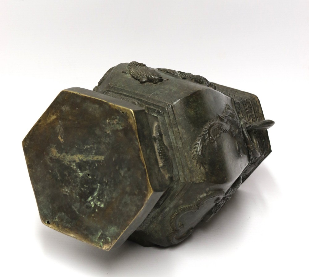 An antique hexagonal solid bronze vessel featuring relief carvings of fish, architectural structures, floral bands, and twin animal-head ring handles. View XII