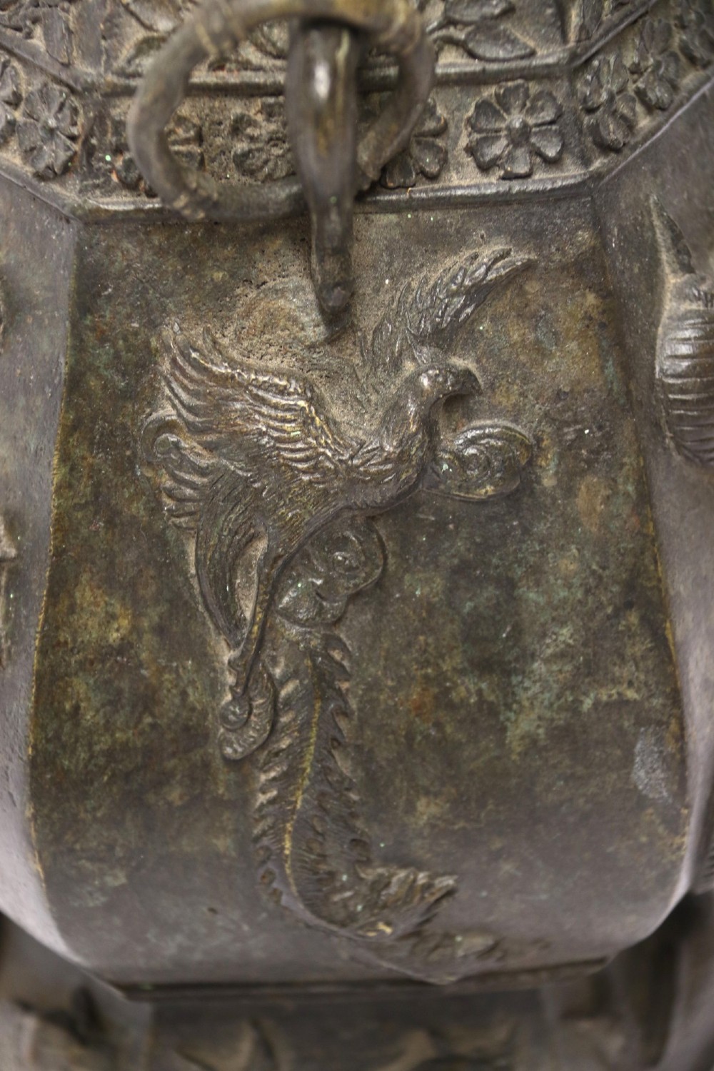 An antique hexagonal solid bronze vessel featuring relief carvings of fish, architectural structures, floral bands, and twin animal-head ring handles. View XV
